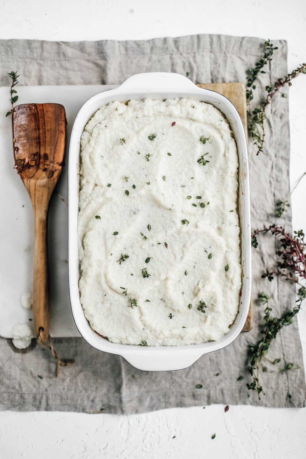 A casserole dish with pre baked shepherds pie and a wooden spatula.