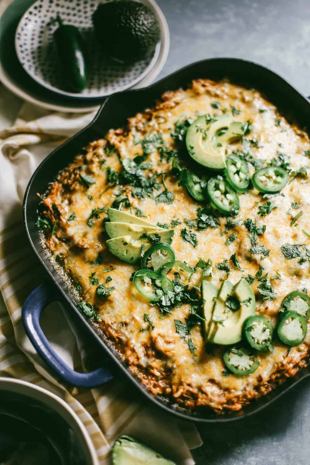 Green Chili Enchilada Cornbread Casserole garnished with sliced avocados and sliced jalapeños.