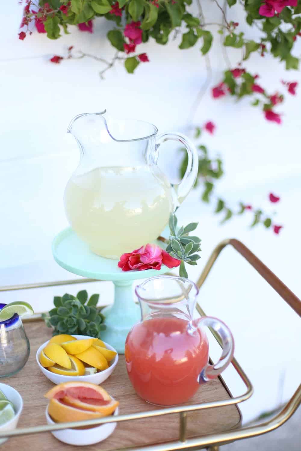 Pitchers of juice with lemon and grapefruit wedges in white bowls on a bar cart