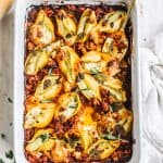 pesto stuffed shells with Italian sausage meat marinara in white casserole dish on white kitchen towel with spoon