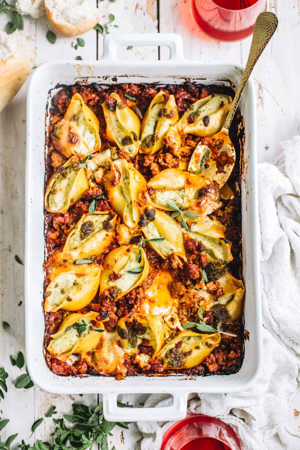 pesto stuffed shells with Italian sausage meat marinara in white casserole dish on white kitchen towel with spoon