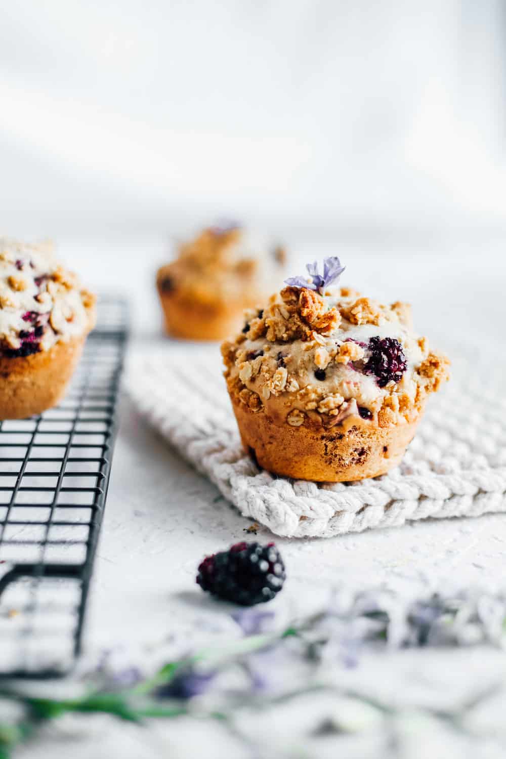 an up close photo of a blackberry rhubarb muffin on a cloth surface with the cooling rack to the left holding more muffins