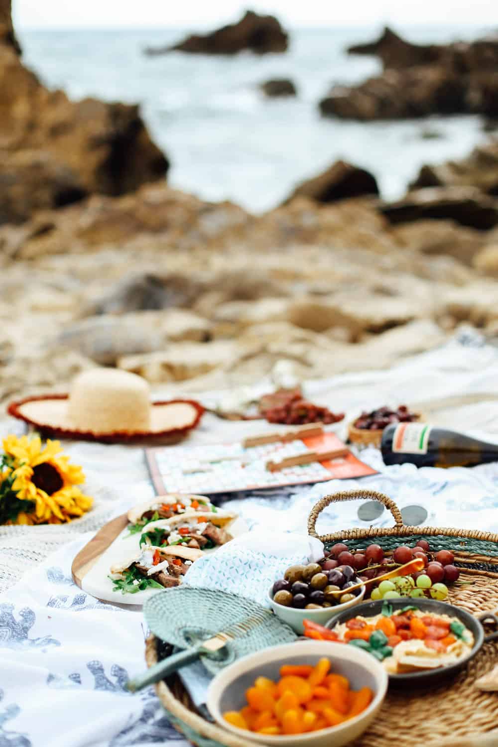 Mediterranean beach picnic spread with lamb pita pockets grapes olives hummus wine and Scrabble game board on beach towels on the beach