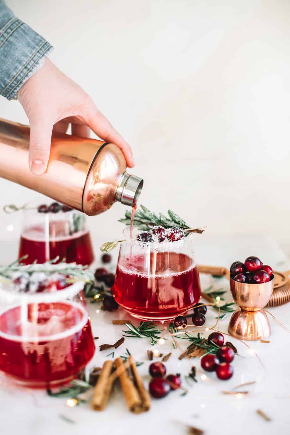 Cranberry whiskey being poured into a low glass garnished with frosted cranberries and a rosemary sprig.