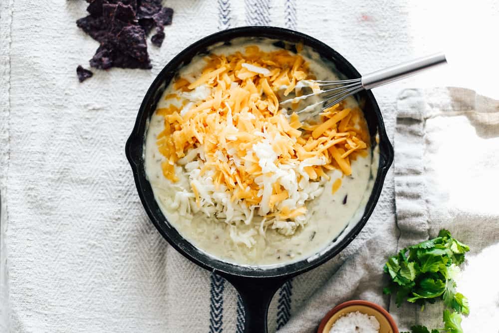 A skillet filled with cheese being whisked. 