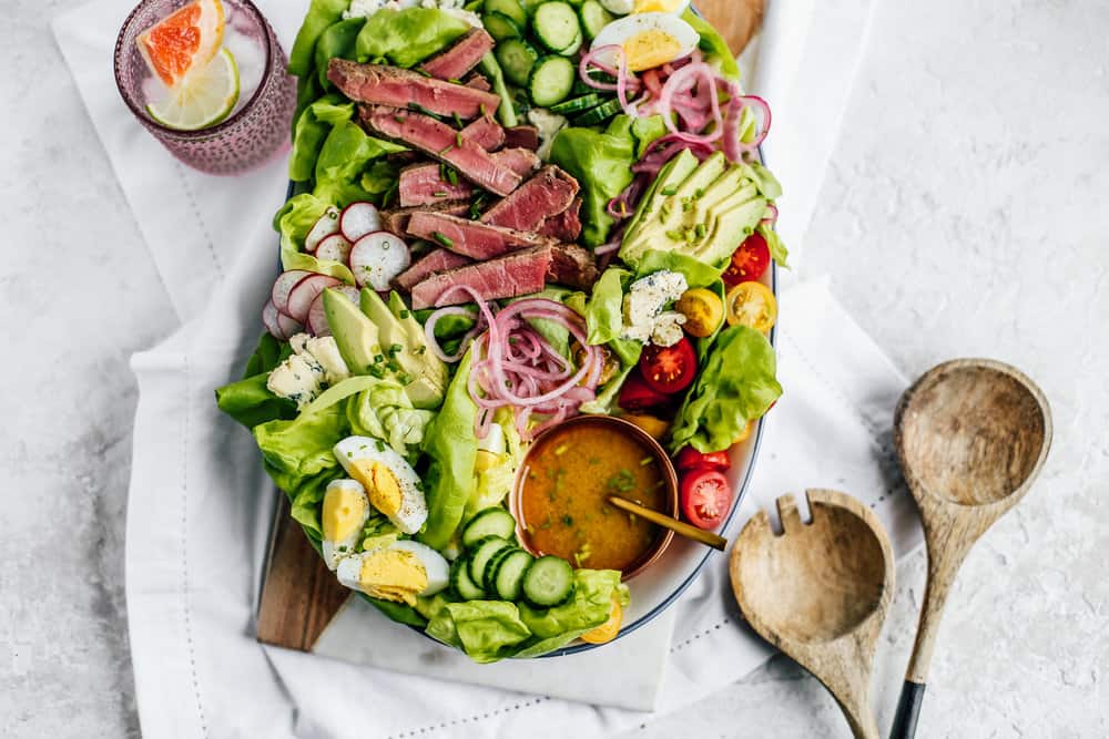 the cobb salad with ahi tuna displayed on a serving board with serving spoons and a drink beside it 