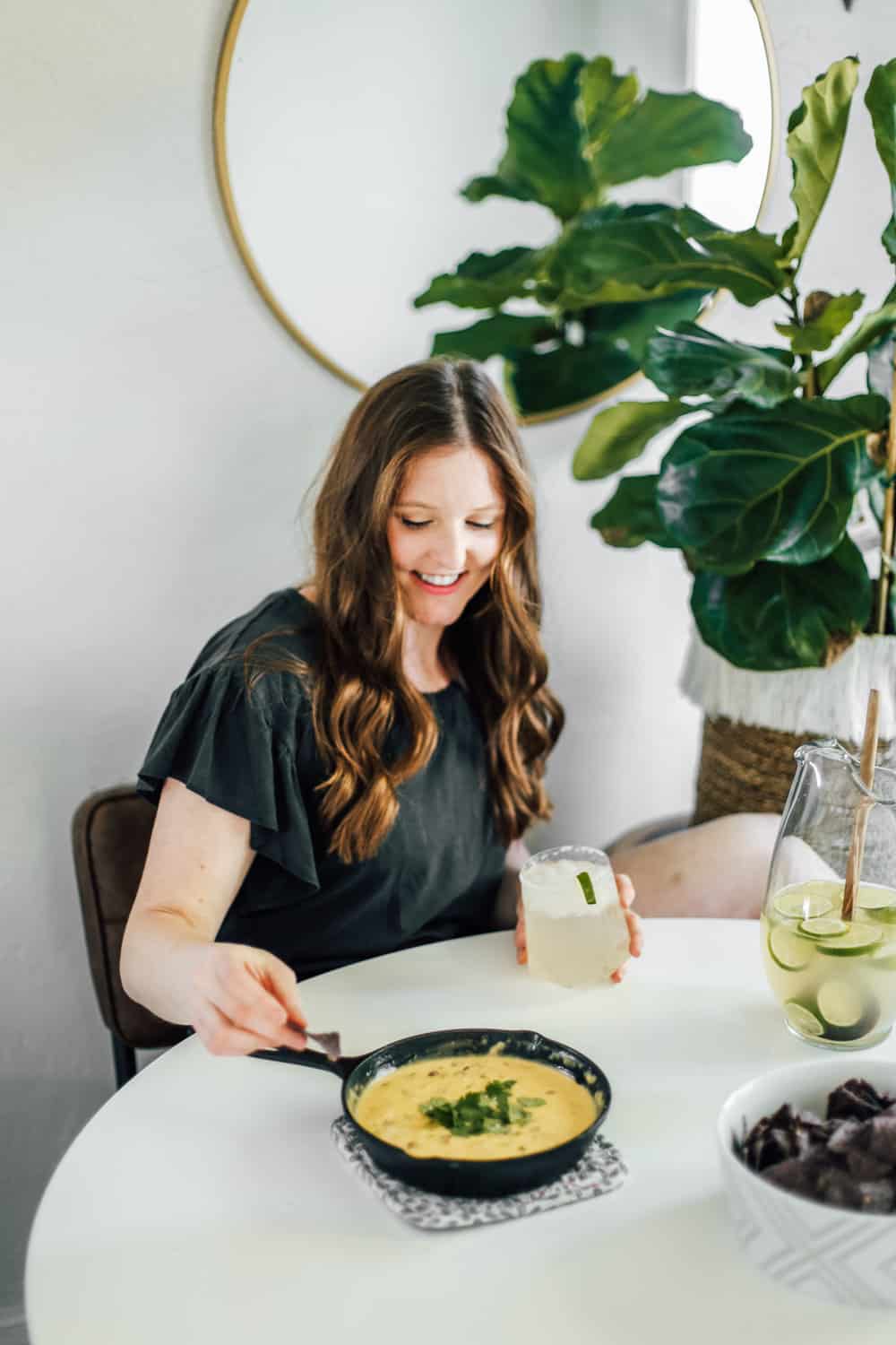 A girl eating green chile queso dip with a margarita in hand. 