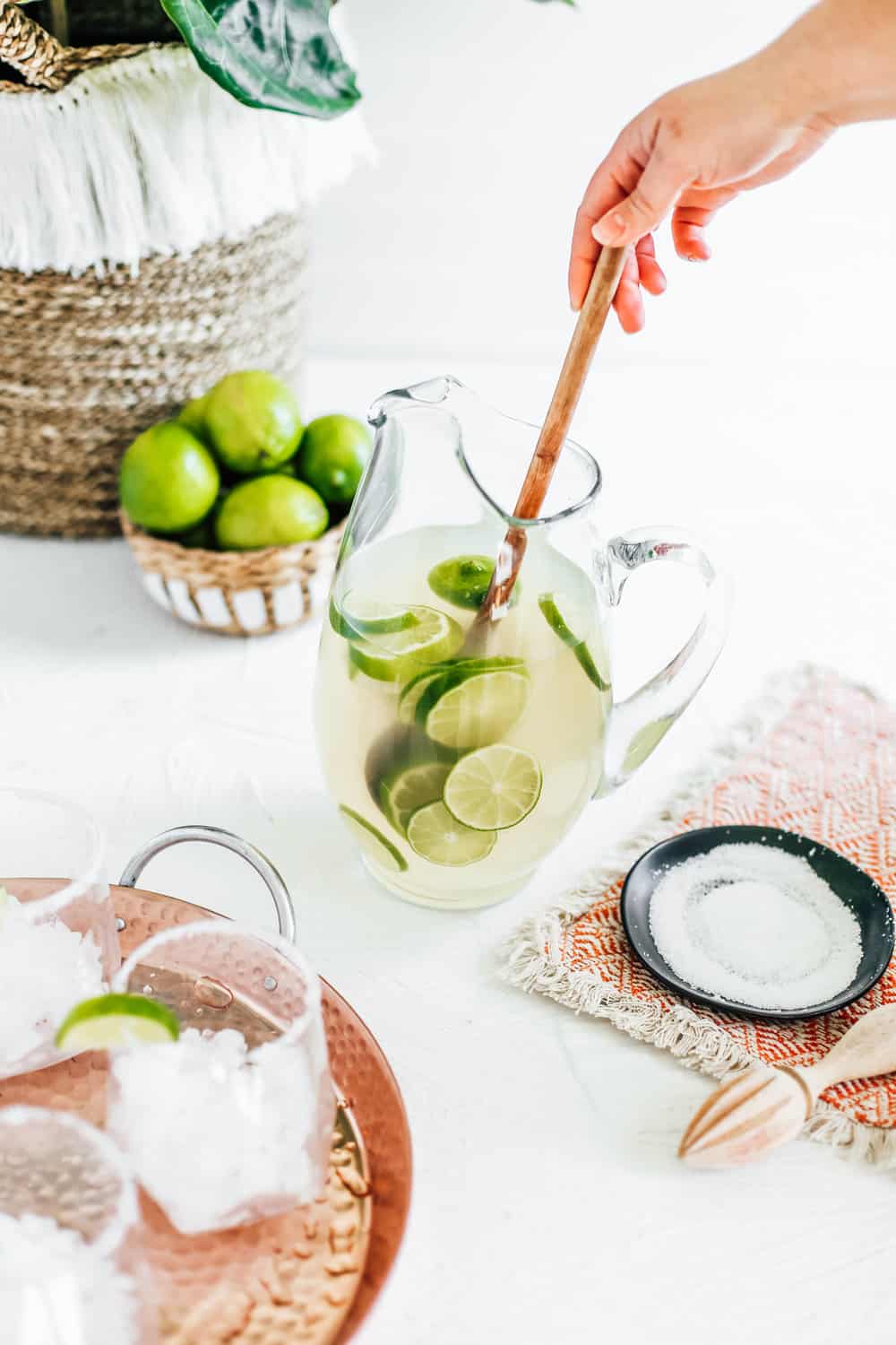 A pitcher filled with a classic margarita with limes and a wooden spoon.