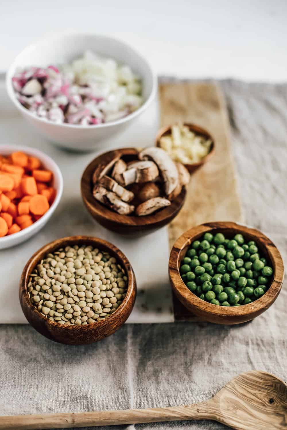 Small wooden bowls of peas, lentils, carrots, mushrooms, and diced onion. 