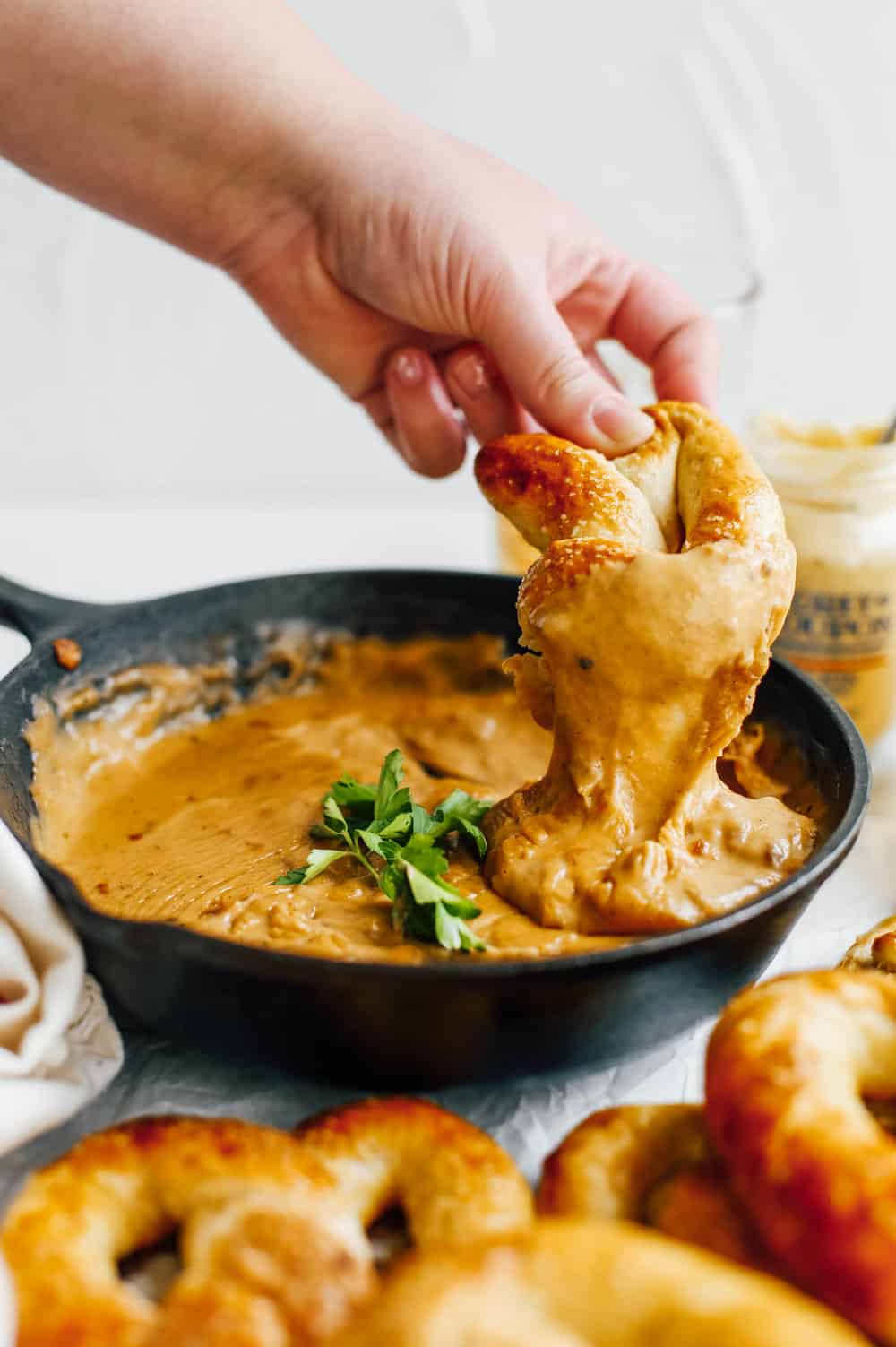 hand dipping soft pretzel in beer cheese dip in cast iron