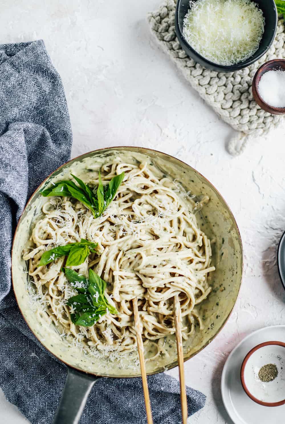 Skinny Fettuccine Pesto Alfredo in skillet with basil leaves and bowl of Parmesan cheese