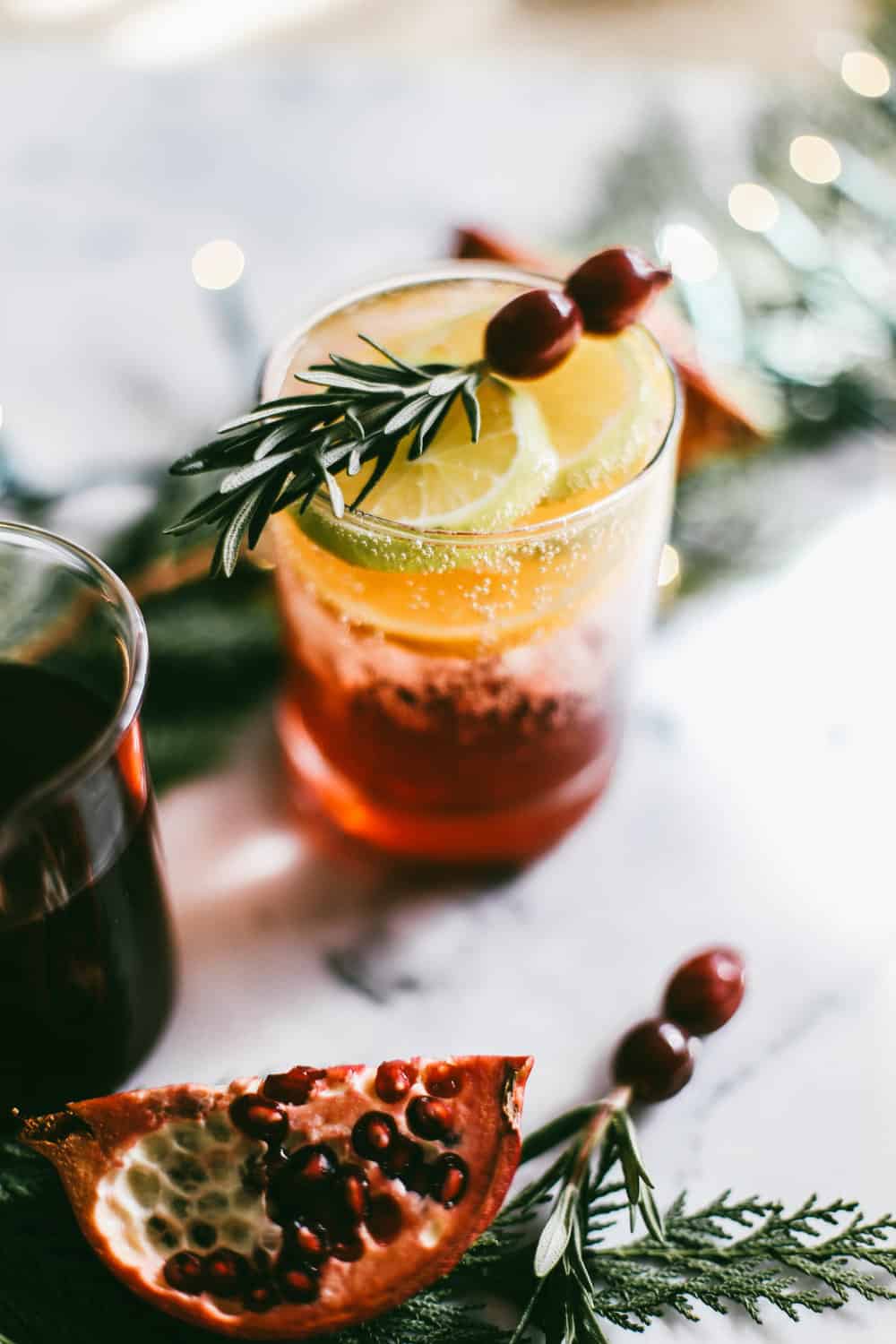 Low glass filled with pomegranate juice and champagne garnished with orange slices, rosemary and cranberries.