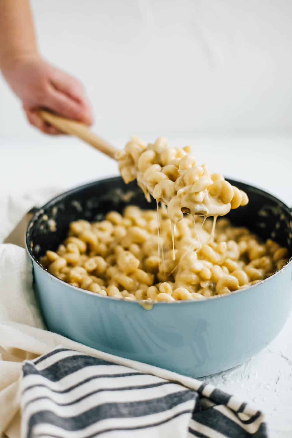 hand holding wooden spoon with creamy mac and cheese in blue pot