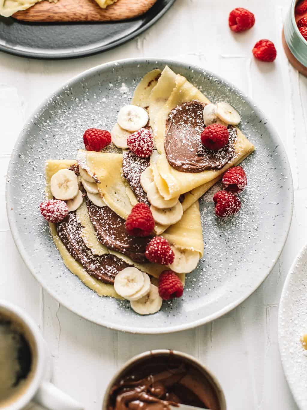 A plate of crepes with Nutella and topped with raspberries and bananas 