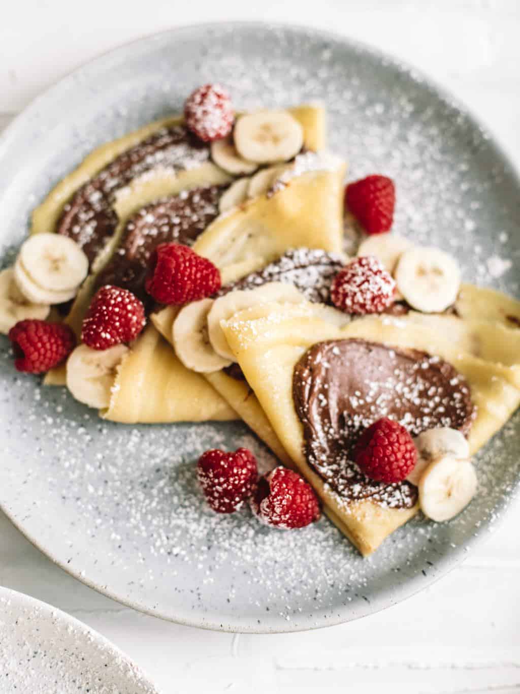 A plate of crepes with nutella, bananas, and raspberries. 