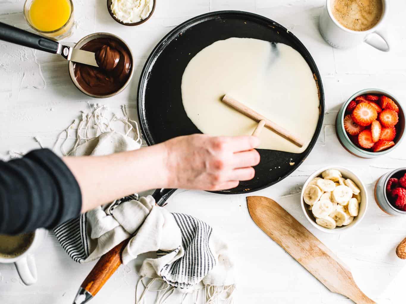 Crepe batter being spread out on a skillet. 