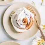 carrot cake cinnamon roll with cream cheese icing on beige plate with gold fork and flowers