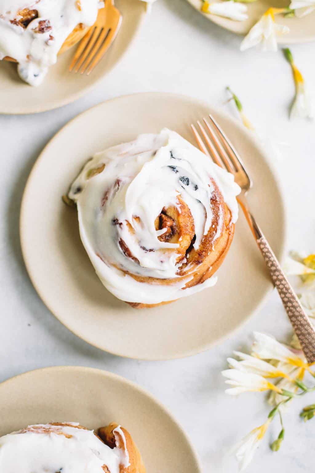 carrot cake cinnamon roll with cream cheese icing on beige plate with gold fork and flowers