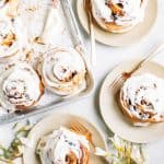 cream cheese glazed cinnamon buns on baking sheet and beige plates