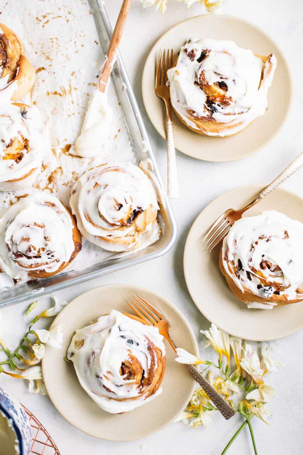 cream cheese glazed cinnamon buns on baking sheet and beige plates