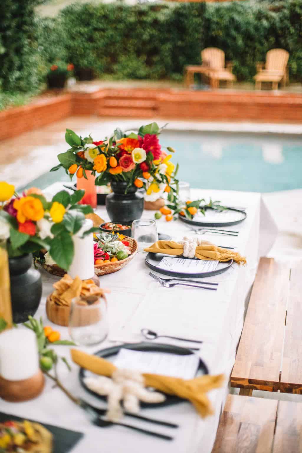 A casual mexican dinner party setting with flowers, table settings and chips.