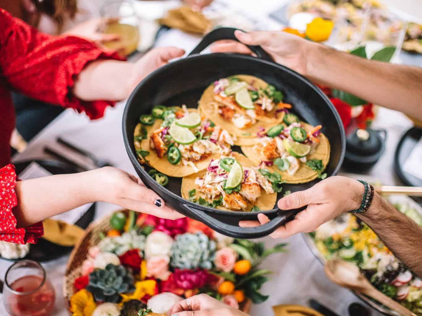 A round black platter of fish tacos being passed across the table.