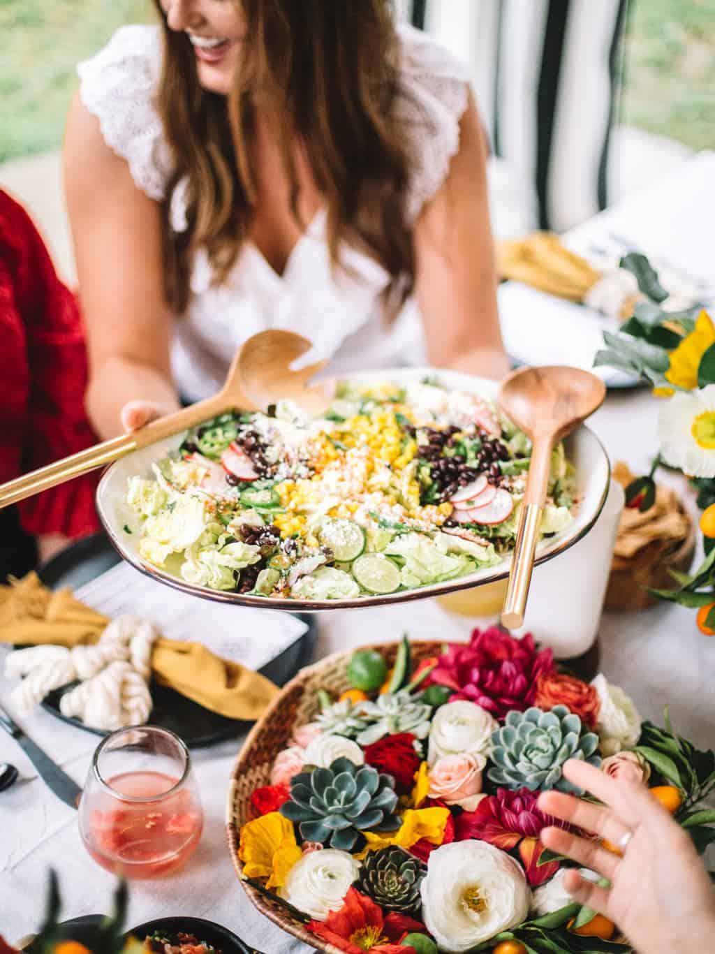 A mexican elote salad platter being passed across the table.