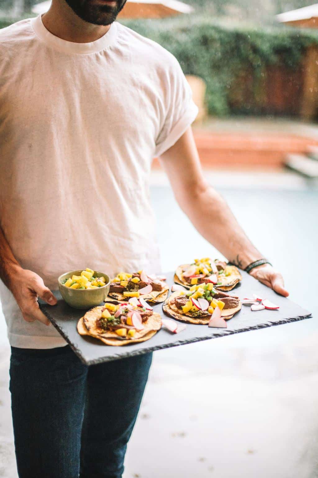 A black slate platter being held with steak tacos topped with mango salsa.