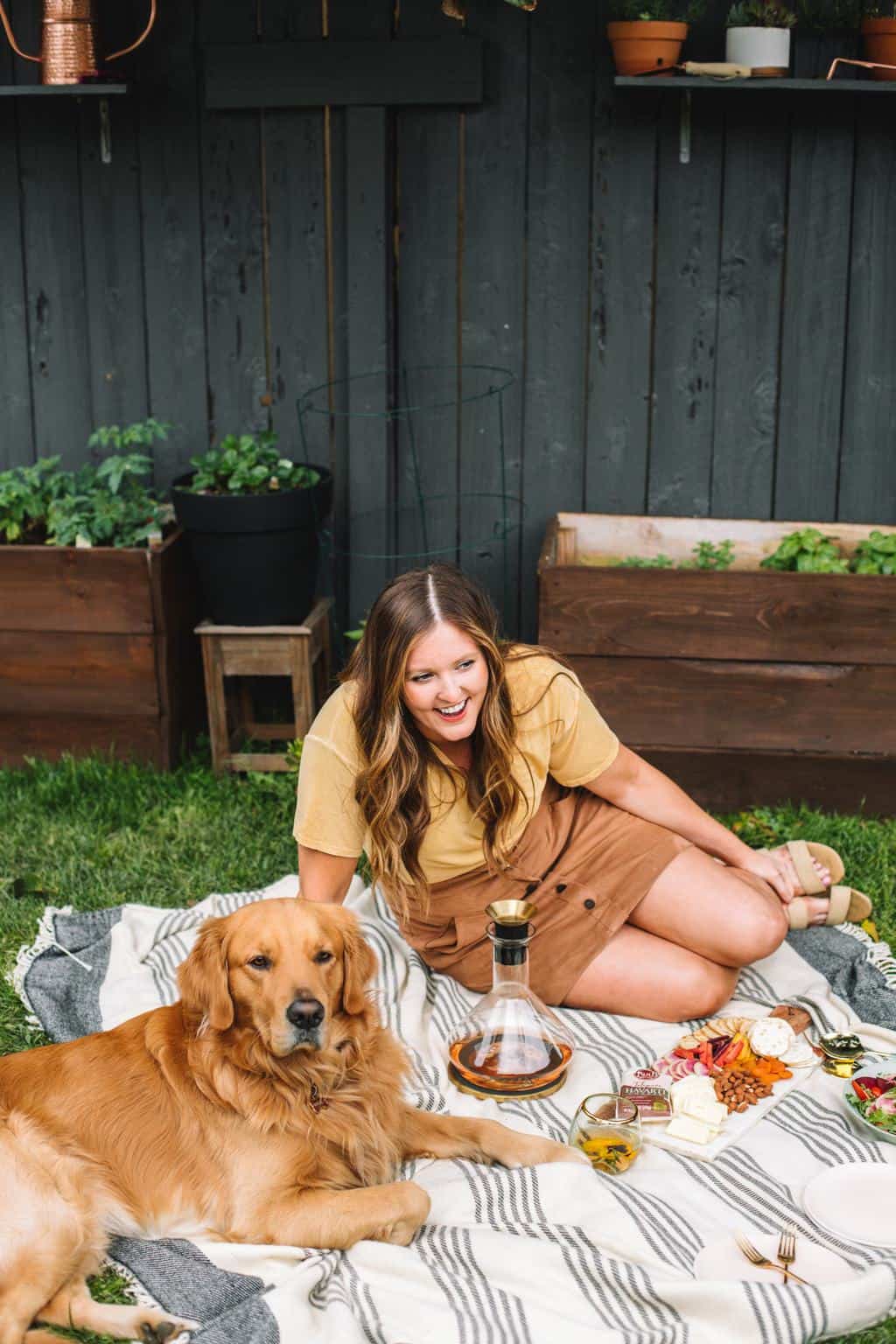 Elizabeth outside on a blanket with rascal, wine, and a cheese board