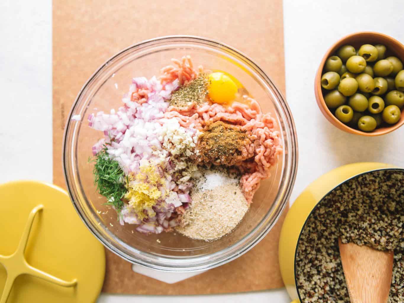 Ingredients for Greek meatballs in a clear bowl with quinoa in a yellow pot