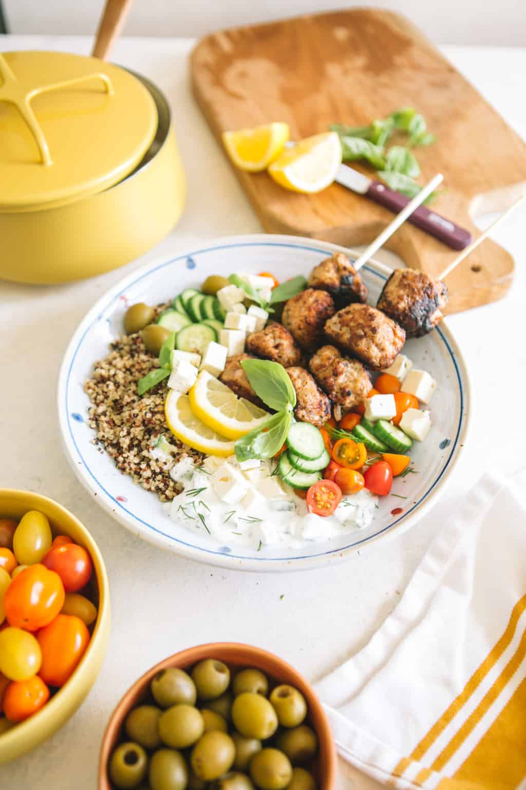 Mediterranean Greek Power Bowls in a white bowl with cherry tomatoes and yellow pot