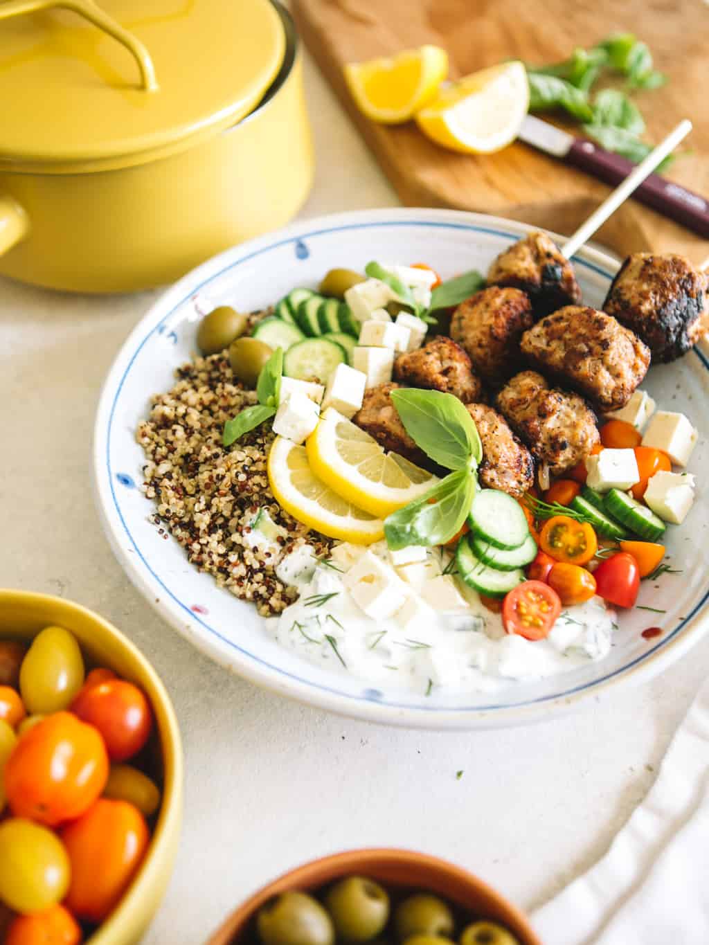 Mediterranean Greek Power Bowls in a white bowl with cherry tomatoes and yellow pot