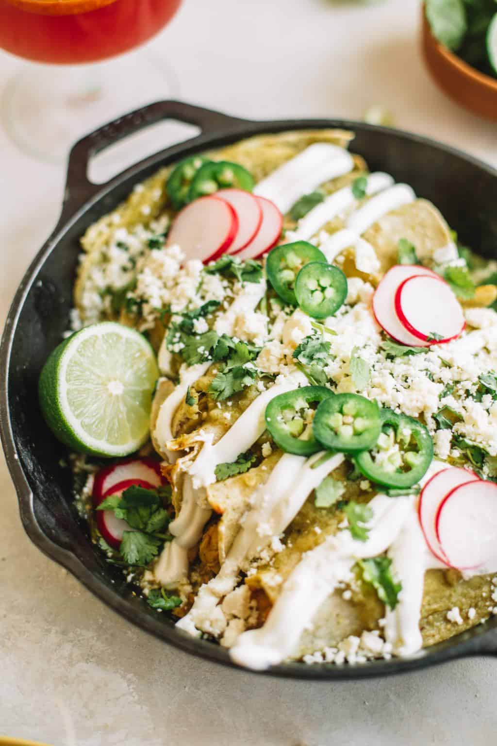 Cast iron skillet filled with green chicken enchiladas