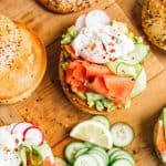 Smoked Salmon bagels with sliced cucumbers and toppings on a wood board