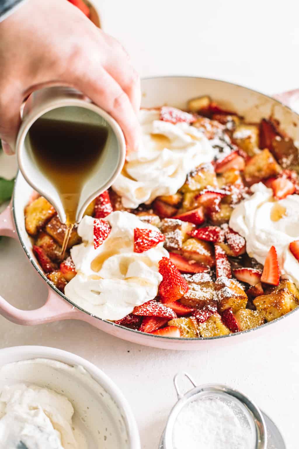 Pouring maple syrup over Strawberry and Cream Overnight French Toast in a pink casserole dish