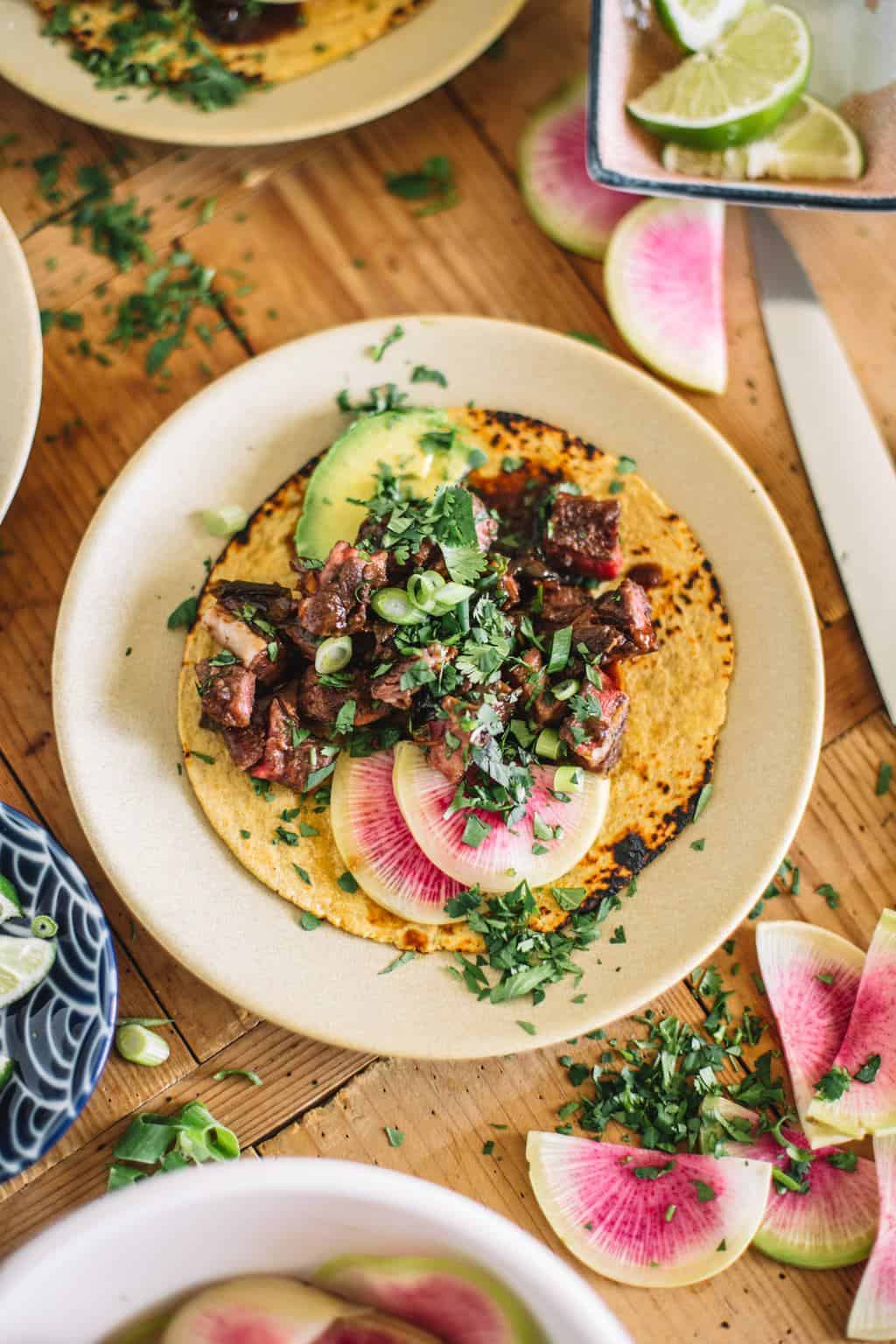 Sous vide Asian short rib tacos on a white plate with toppings