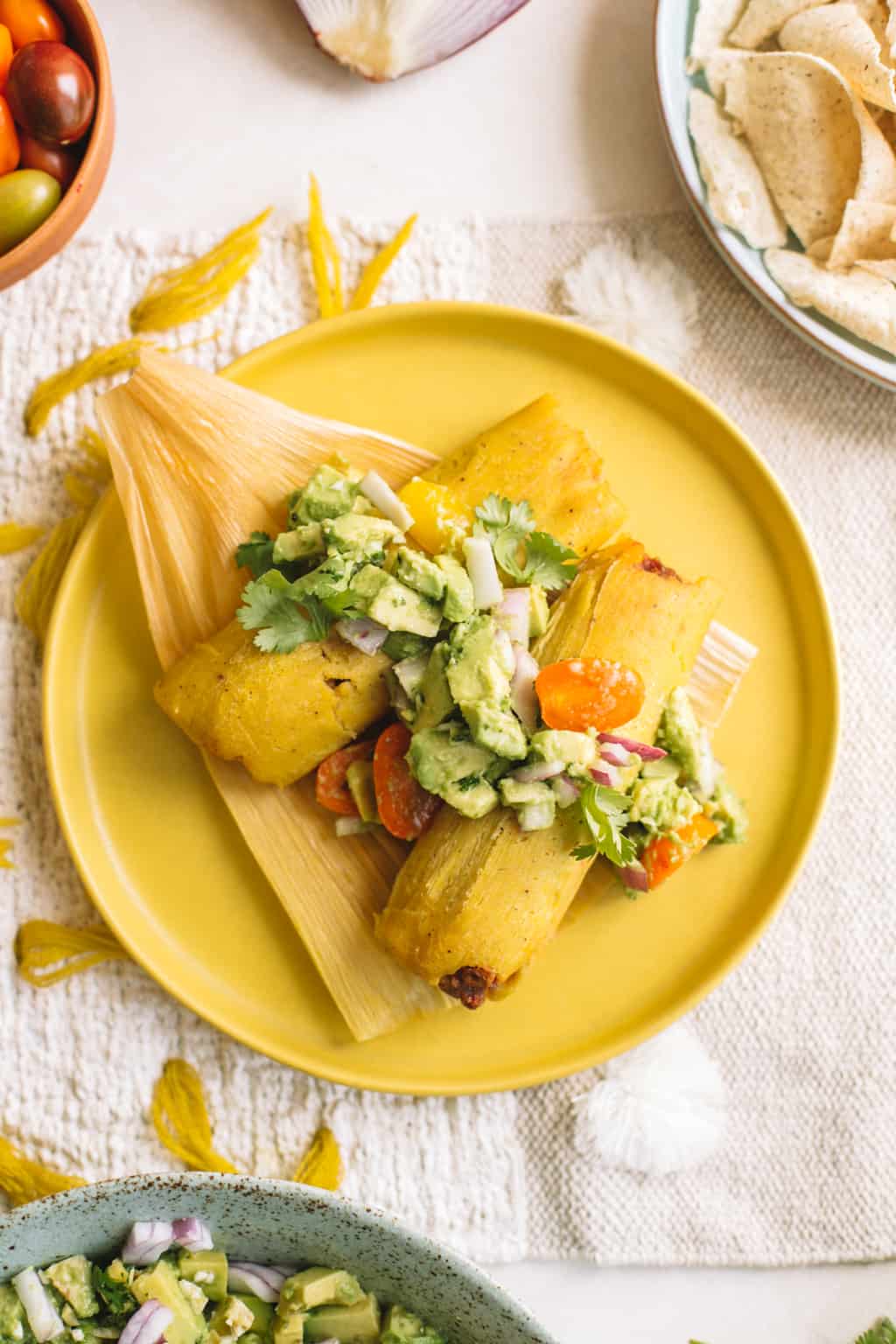 A yellow plate topped with tamales and deconstructed avocado salad.