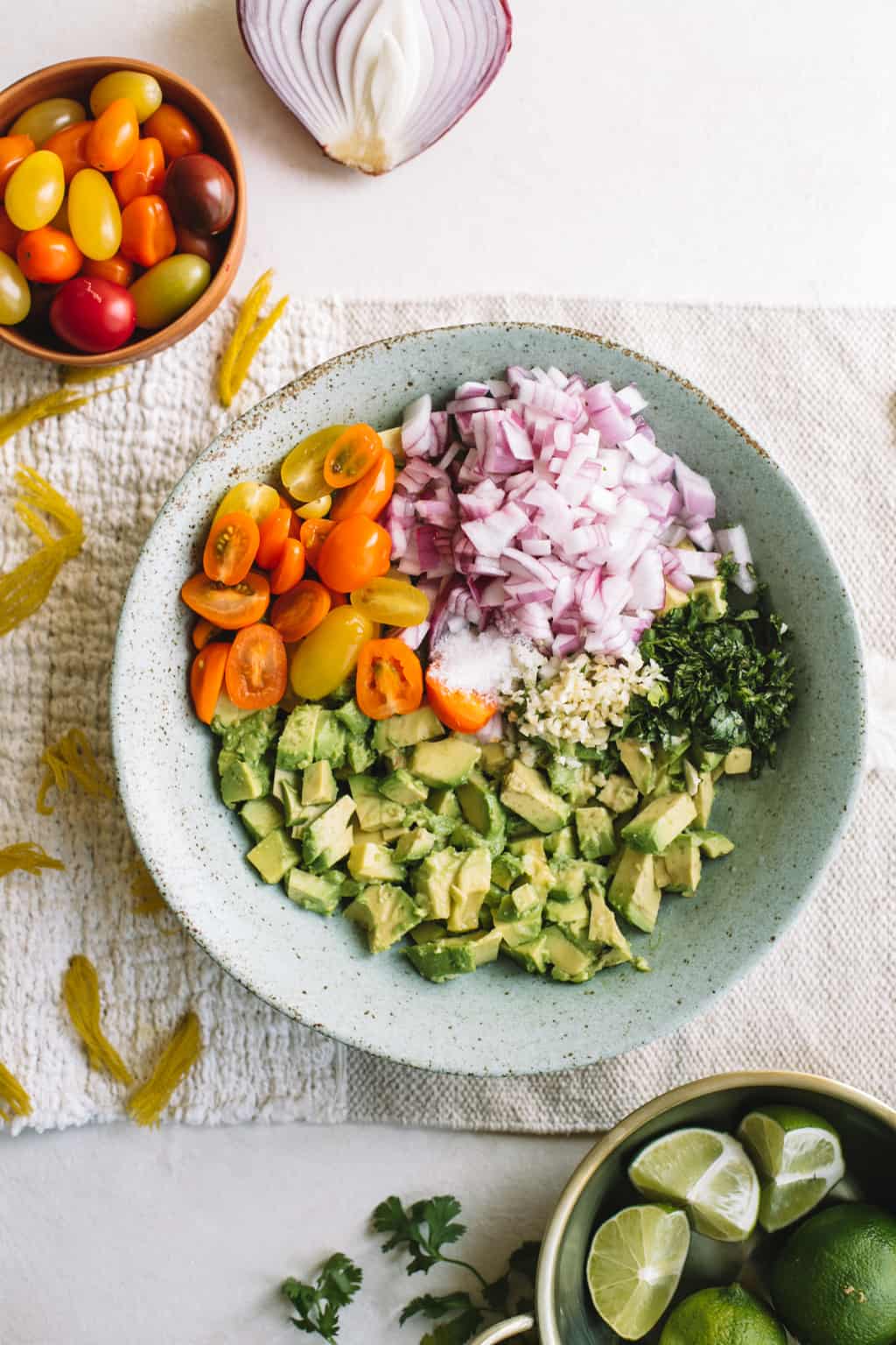 Blue bowl filled with avocado chunks, cilantro, red onion and heirloom cherry tomatoes.