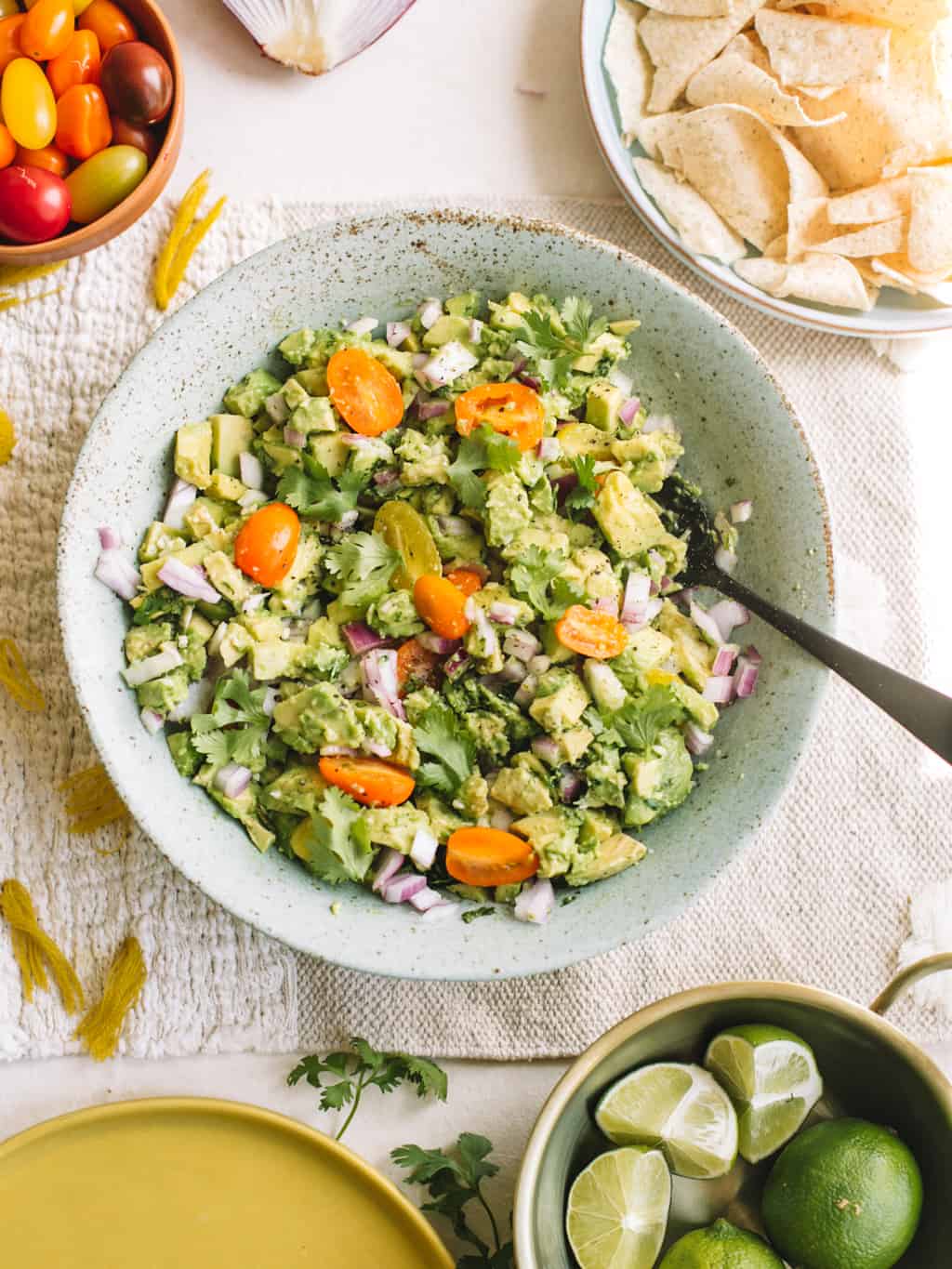 Blue bowl filled with avocado, heirloom tomatoes, cilantro, red onion and lime.