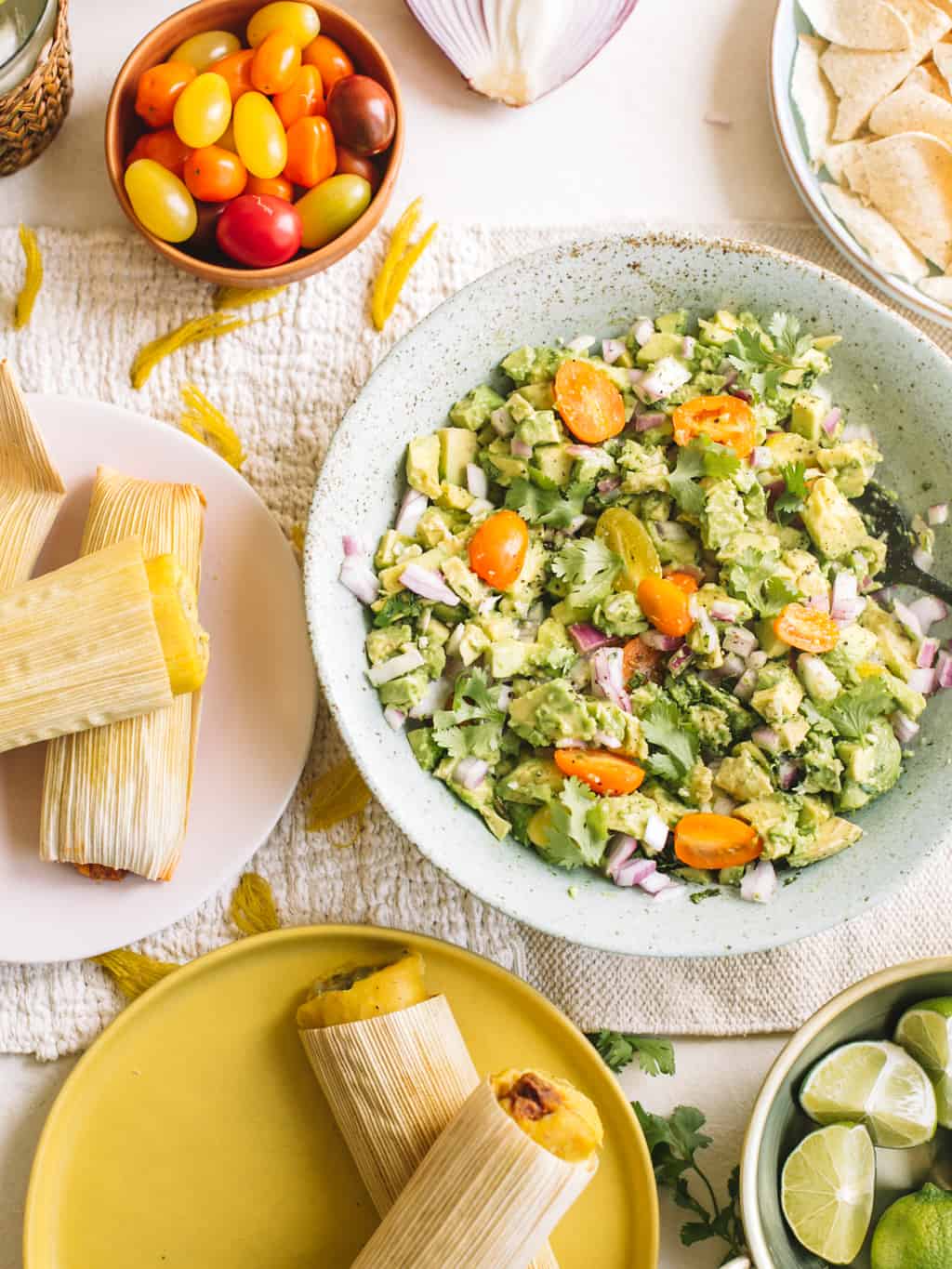 Blue bowl filled with deconstructed avocado salad and a side pink plate of tamales.