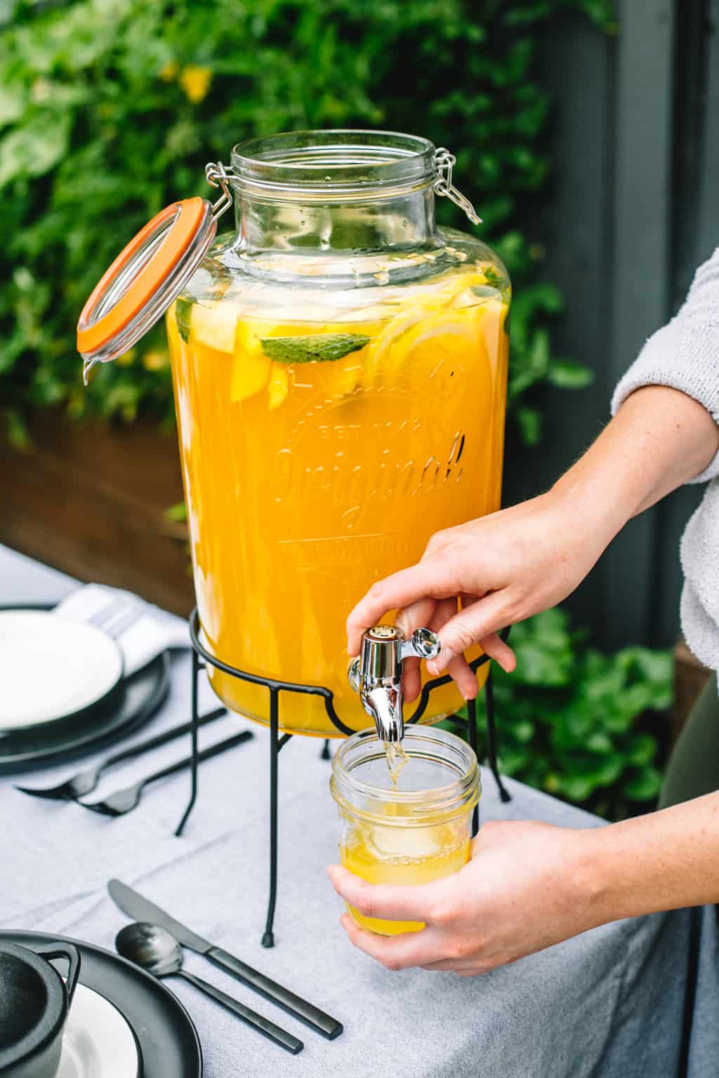 Beverage dispenser full of mango lemonade being poured into a mason jar. 