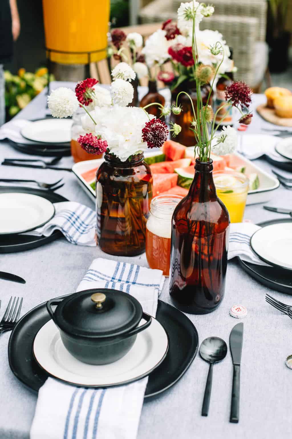 Black dinner plate with a white salad plate and a black cast iron cocotte on top of a fathers day bbq tablescape.