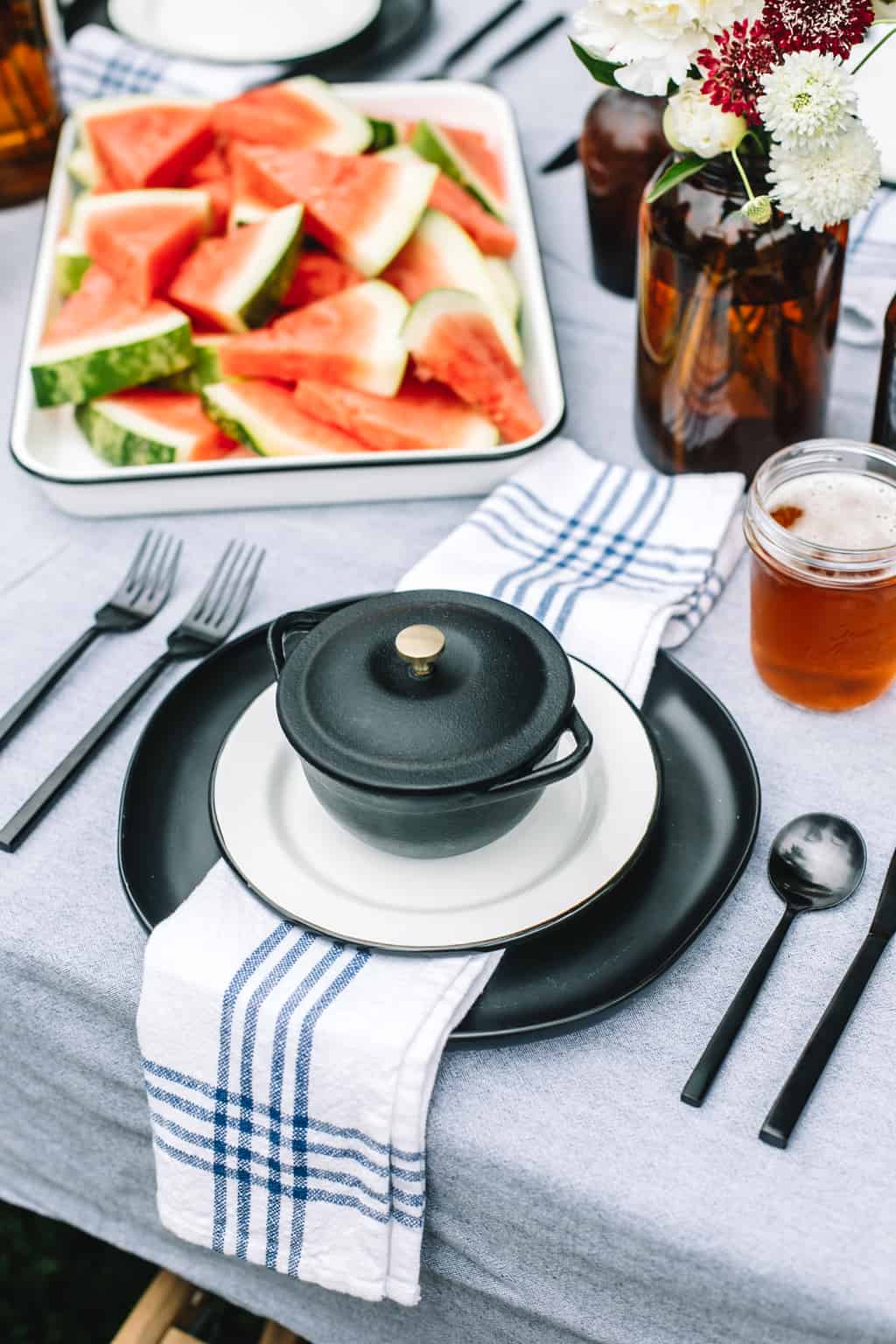 Black plate with a blue and white napkin and a platter of watermelon.