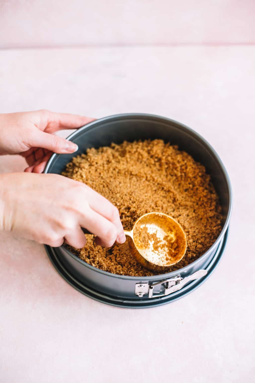 Graham cracker crust being patted down in a silver spring form pan