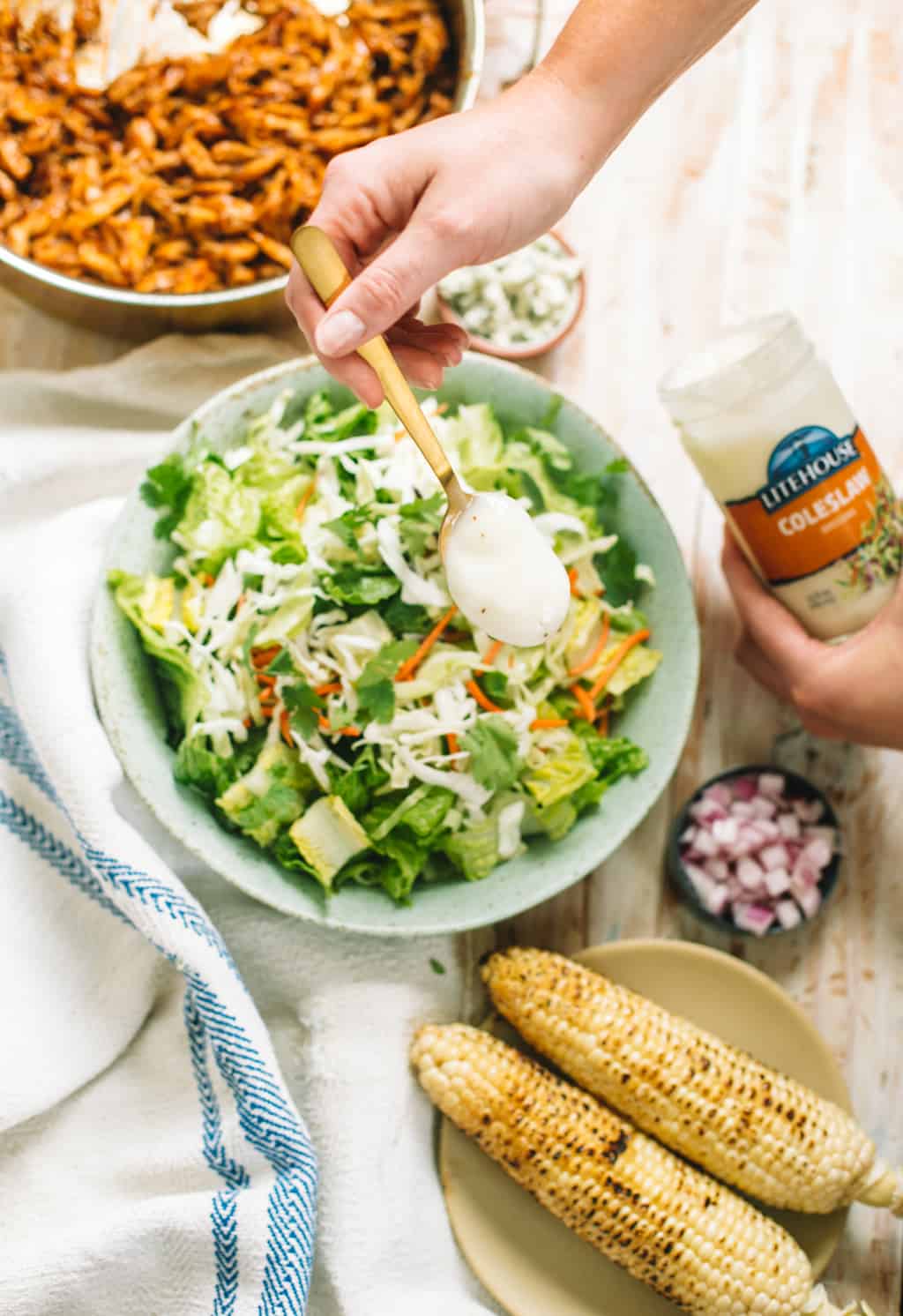 Coleslaw dressing being drizzled onto salad slaw mixture in a blue bowl.