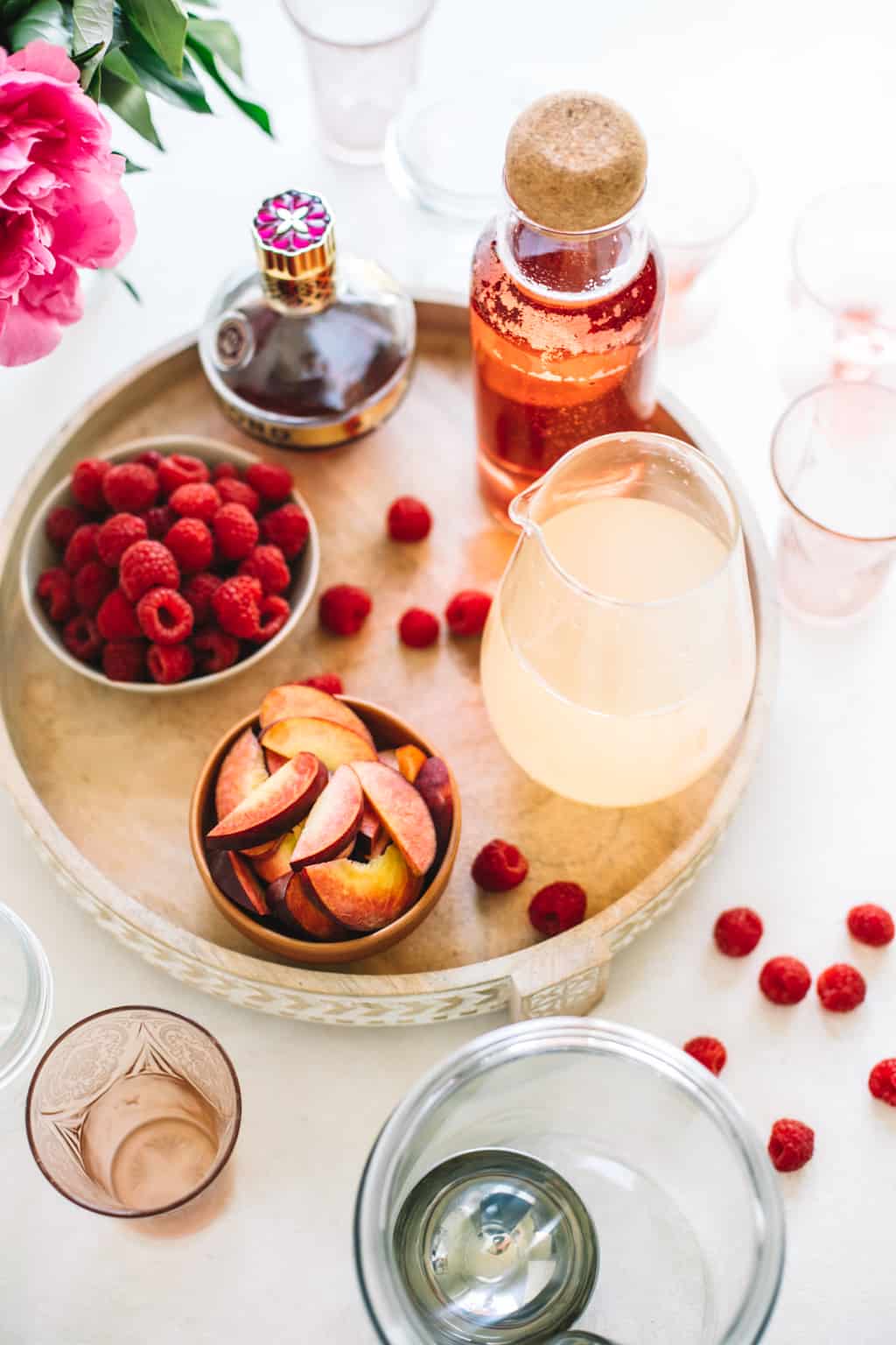 Fresh raspberries, fresh peach slices, lemonade in a pitcher, rosè in a pitcher and chambord on a wooden serving platter.