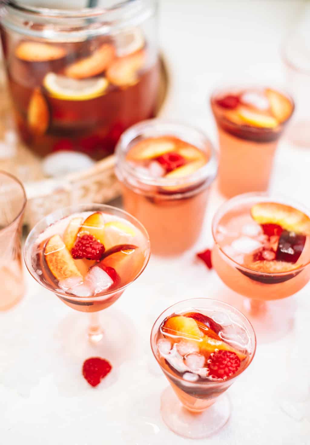 Rosè sangria with peaches and raspberries served in pink wine glasses. 