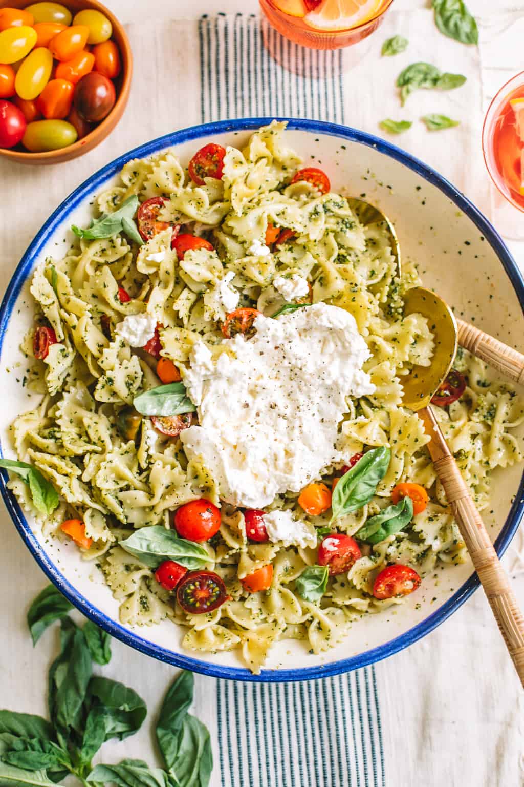 Pesto pasta salad in a white bowl with blue rim with burrata cheese and two spoons