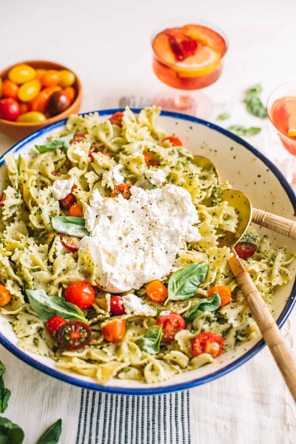 Pesto pasta salad in a white bowl with blue rim with burrata cheese and two spoons