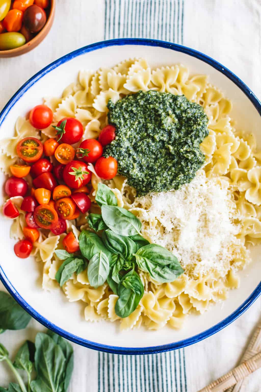 Pasta, pesto, tomatoes, Parmesan, and basil in a white bowl with blue rim